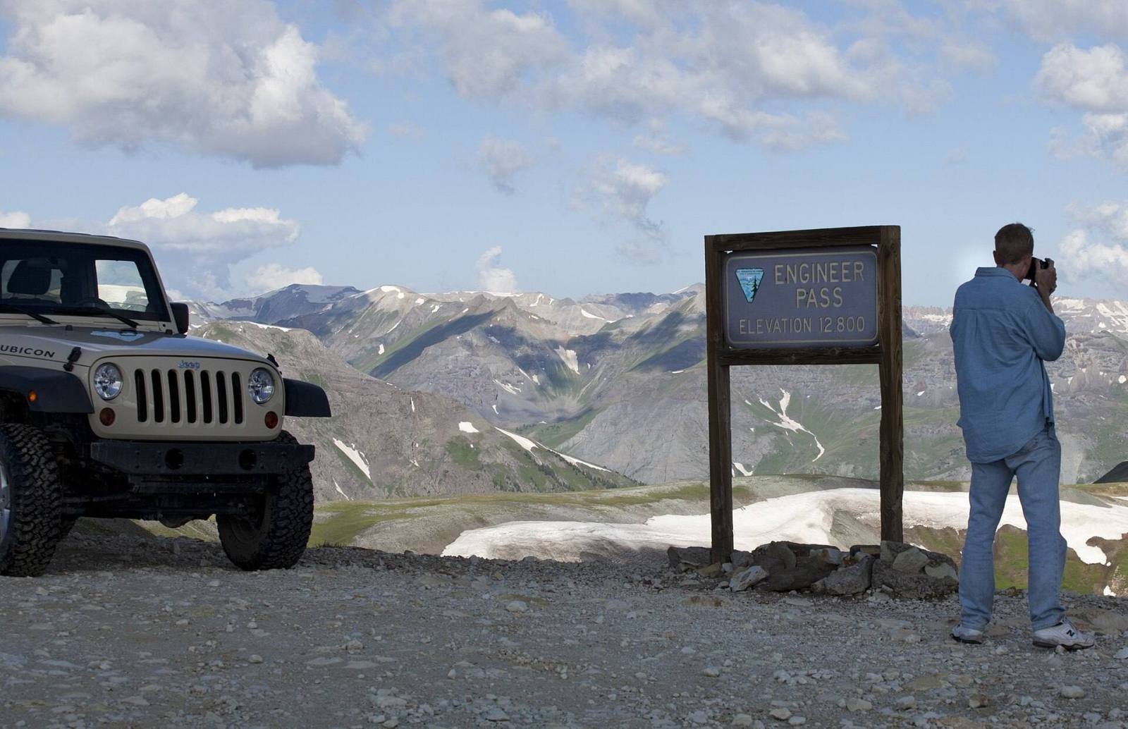 A jeep parked beside a trail sign at a high pass in the San Juan Mountains