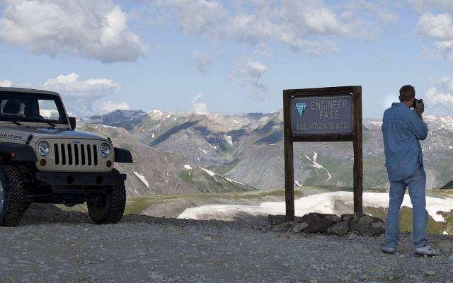 A jeep parked beside a trail sign at a high pass in the San Juan Mountains