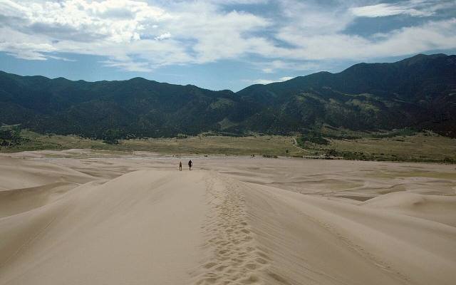 Walkers on the crest of a sand dune with the Sangre de Cristo Mountains beyond