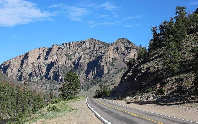 Highway 149 curving below a tall cliff of volcanic tuff near Creede