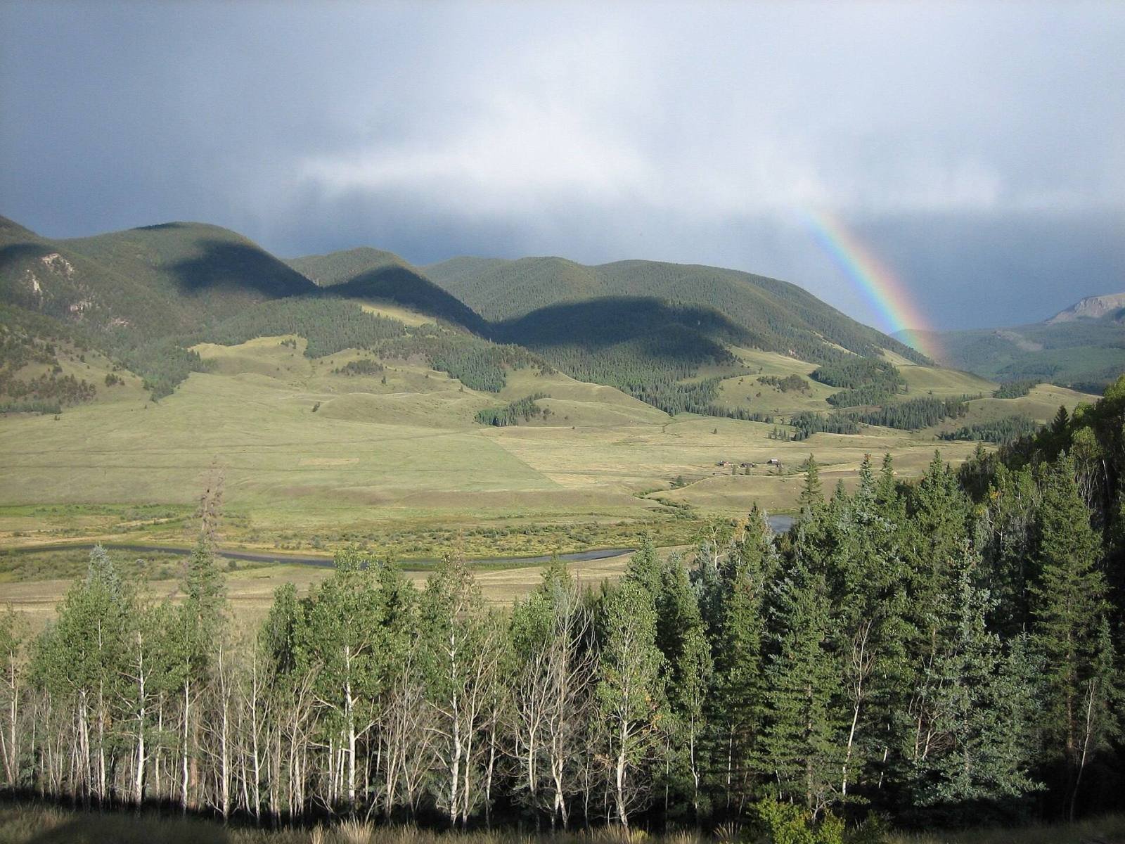 The upper Rio Grande winding through a green valley near Creede under a rainbow