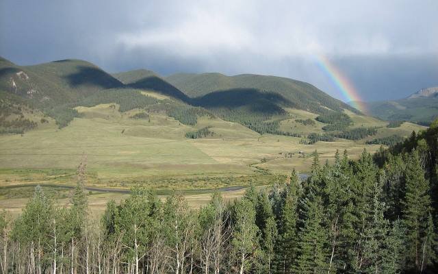 The upper Rio Grande winding through a green valley near Creede under a rainbow