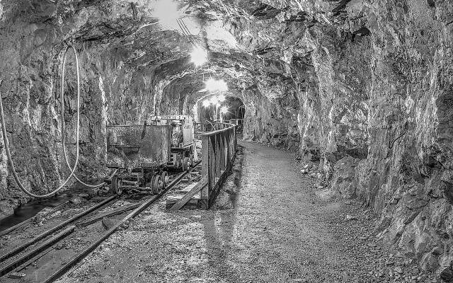 Mine tracks and a rail car in a lit tunnel of the Old Hundred Gold Mine