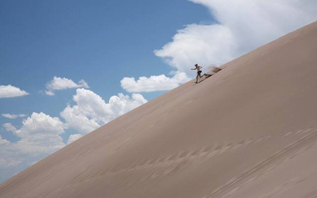 A visitor running down a steep sand dune under a blue sky